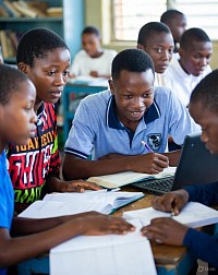 An engaging photo of Kenyan students using study materials and a laptop with books